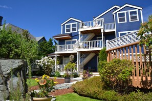 A two-story house with a balcony, a stone wall, and a garden with flowers and shrubs. - The Heron Inn & Day Spa (La Conner)