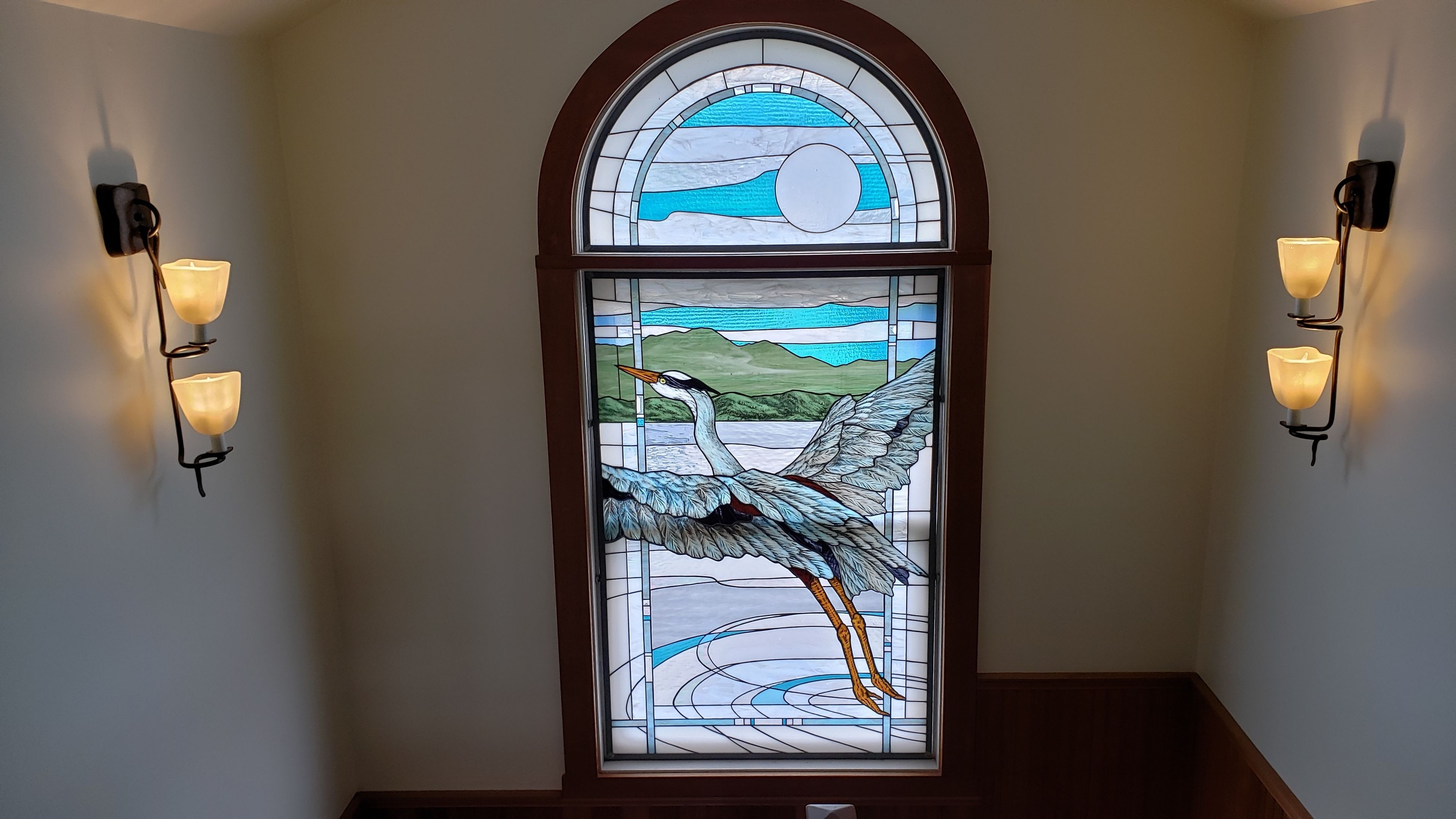 A stained glass window with a crane design, flanked by wall-mounted lights.