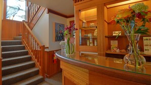A hotel lobby with a wooden staircase, a reception desk with glass top, and a display of flowers. - The Heron Inn & Day Spa (La Conner)