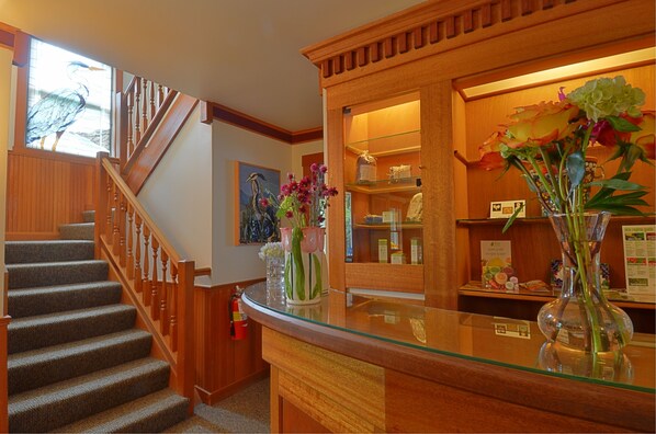 A hotel lobby with a wooden staircase, a reception desk with glass top, and a display of flowers. - The Heron Inn & Day Spa (La Conner)
