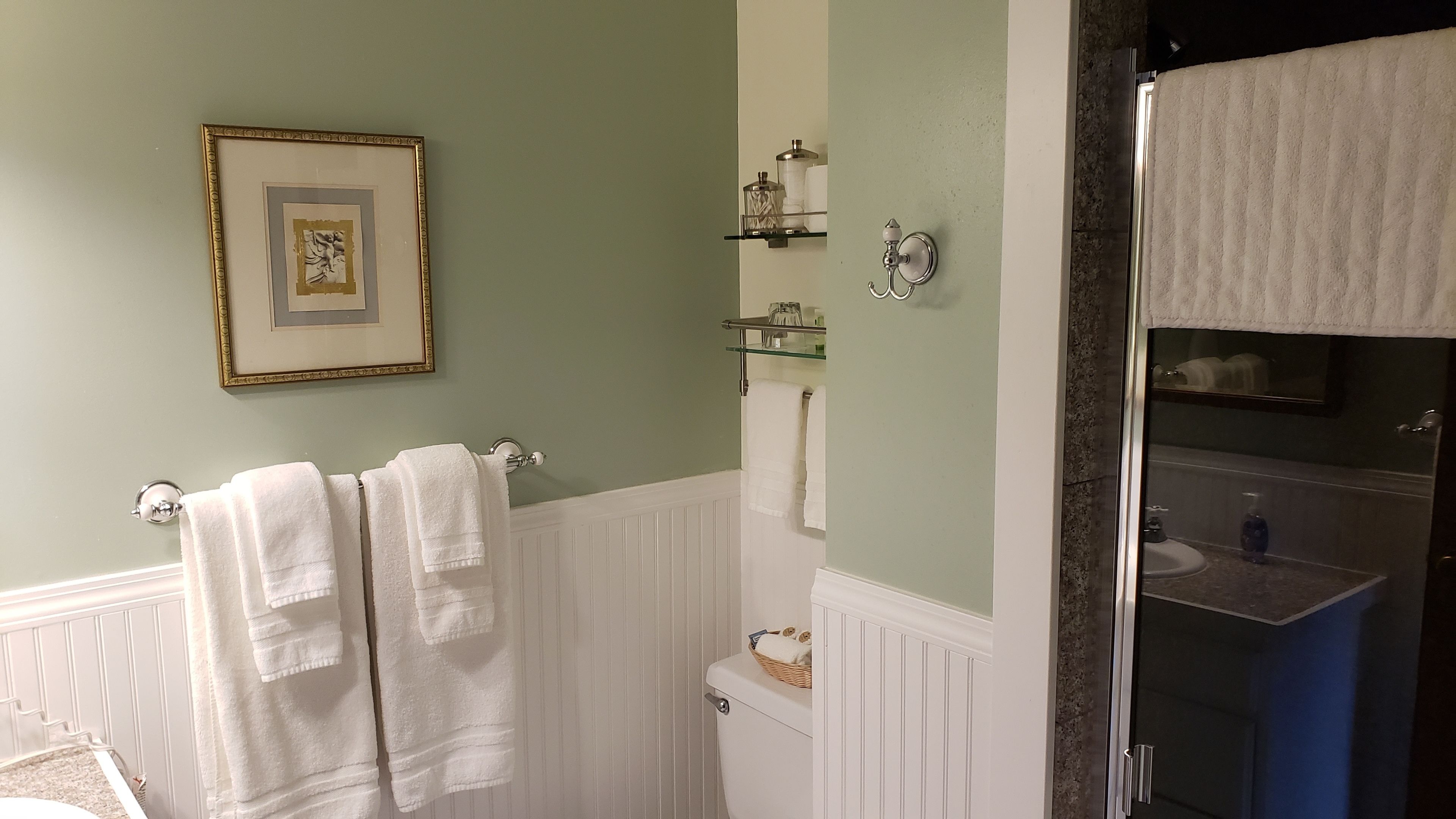 Ein Badezimmer mit Toilette, Waschbecken und Duschbereich. Handtücher hängen an einem Wäscheständer und ein gerahmtes Bild ist an der Wand angebracht.