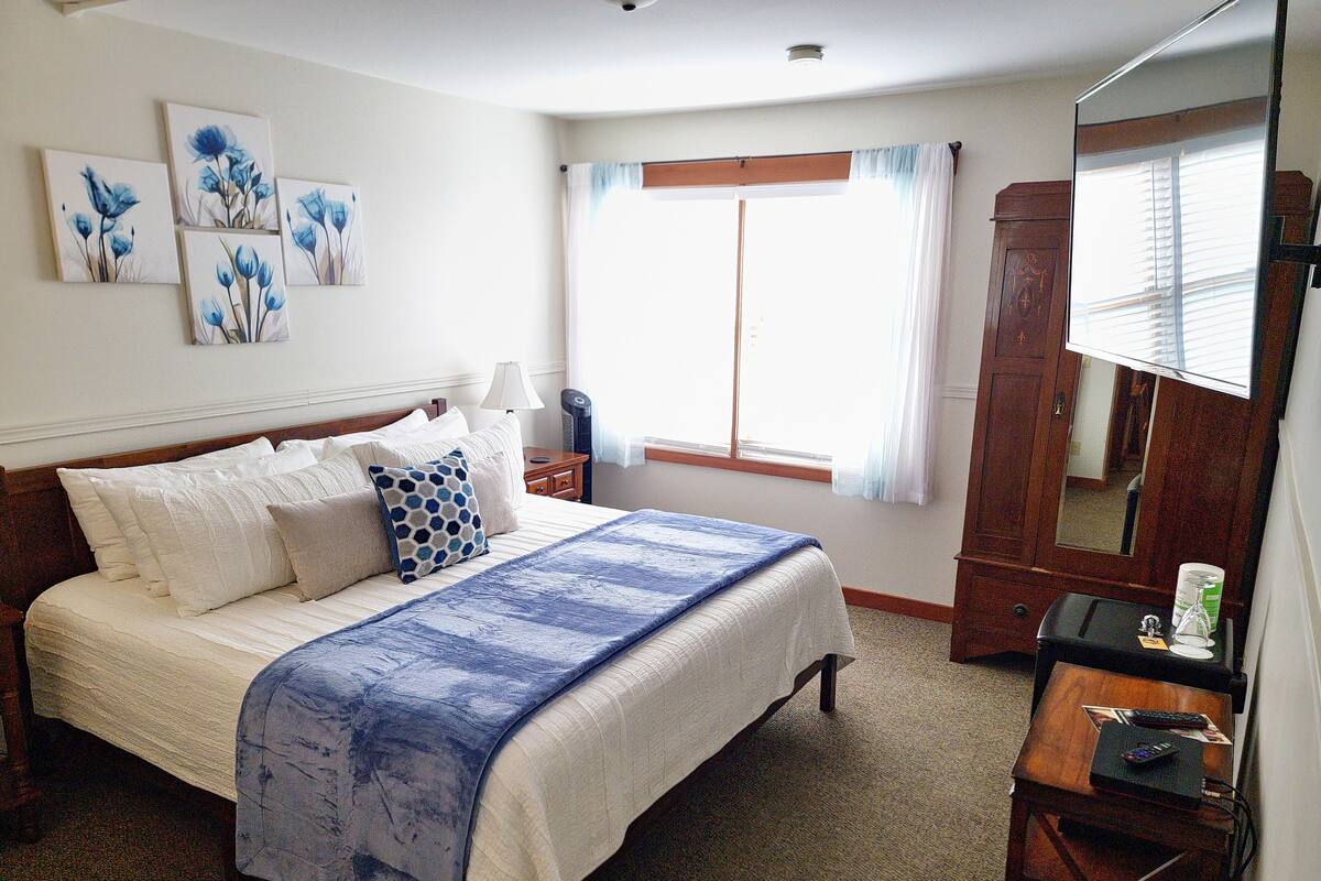 A bedroom with a bed, a nightstand, a dresser, a mirror, and artwork on the wall.