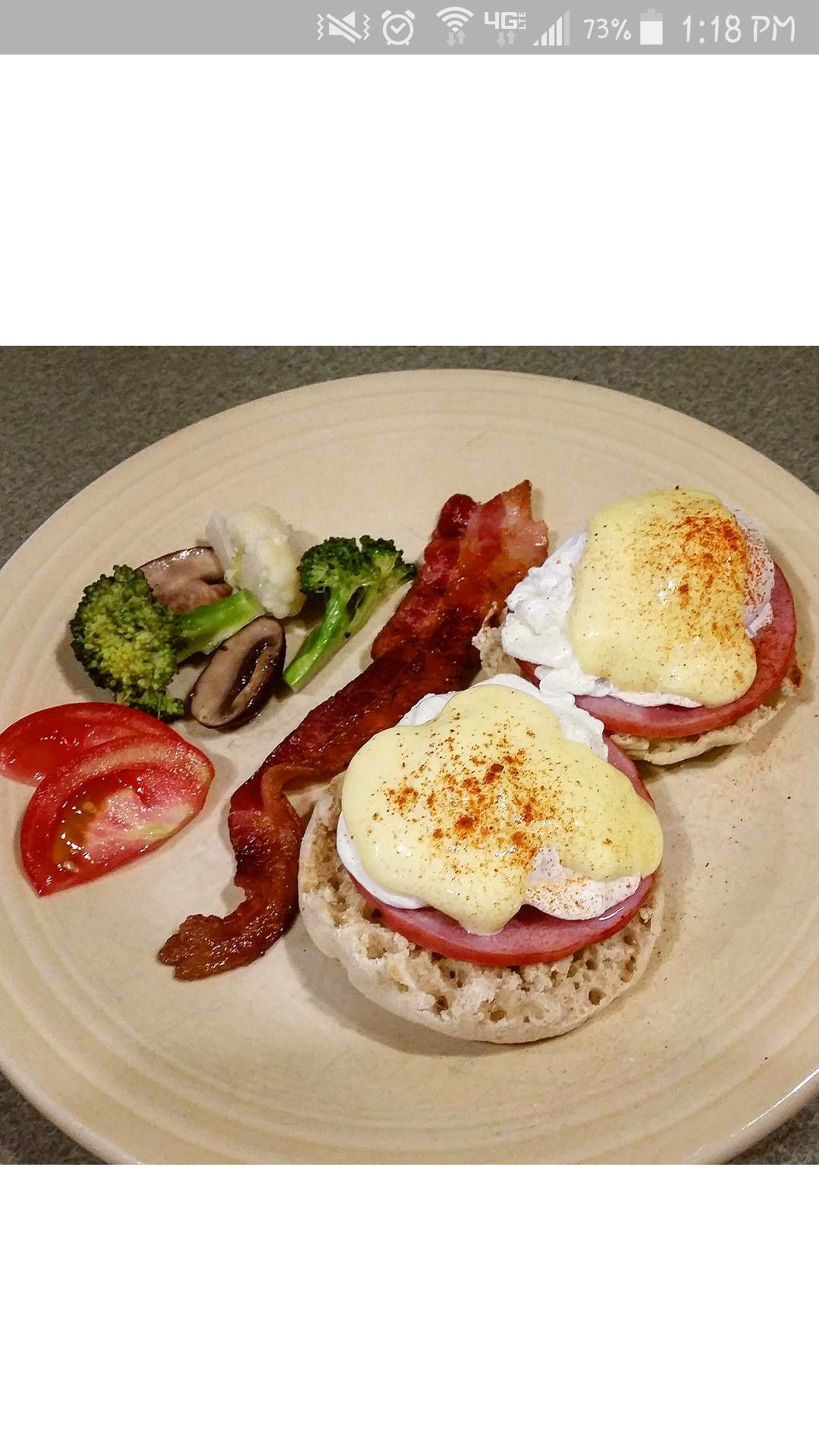 A plate with eggs benedict, bacon, tomatoes, and broccoli.