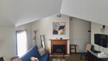 A living room with a blue sofa, a fireplace, a television, and a painting on the wall.