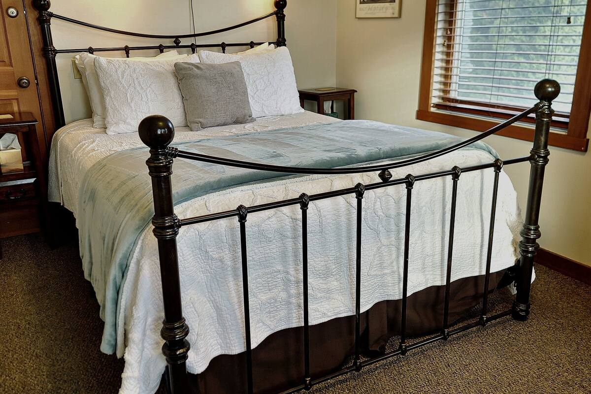 A bedroom with a four-poster bed, a nightstand, a bedside table, and a window with blinds.