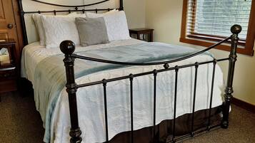A bedroom with a four-poster bed, a nightstand, a bedside table, and a window with blinds.