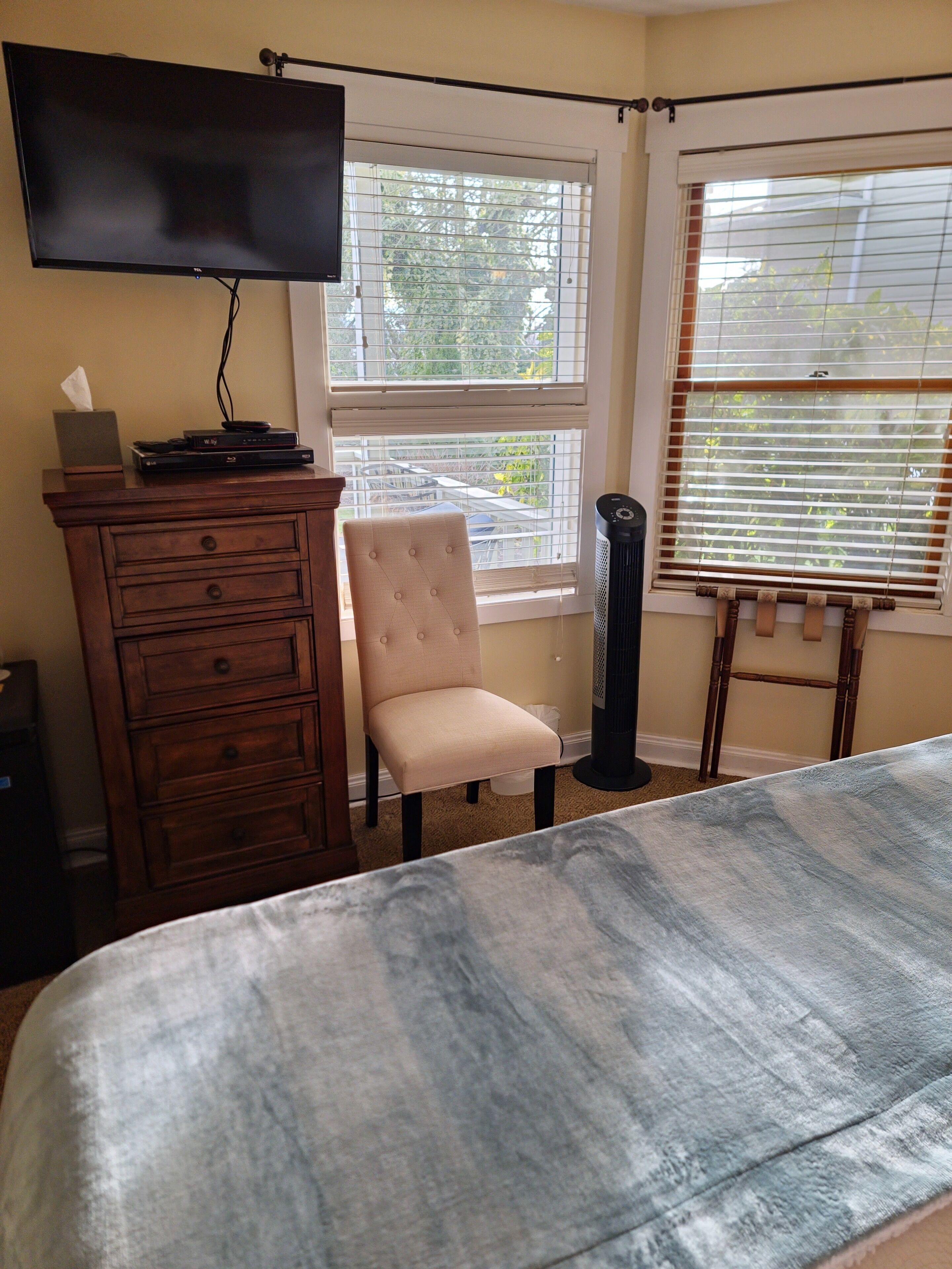 Una camera da letto con un letto, una TV a parete, una sedia, una cassettiera e una finestra con persiane.