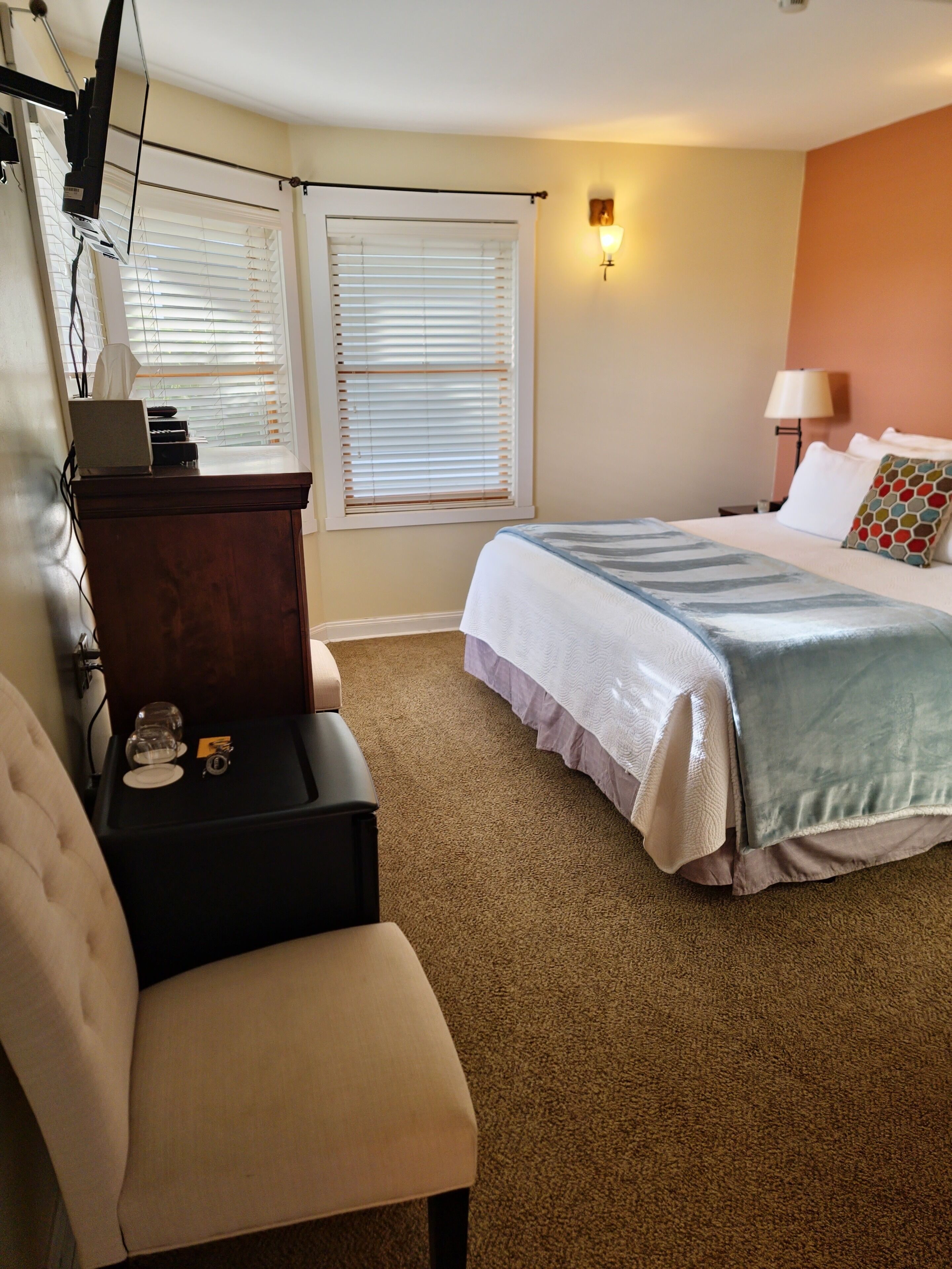 A hotel room with a bed, a desk, a chair, and a lamp.