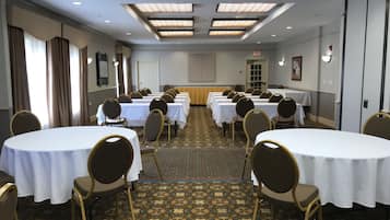 Un salón de conferencias con varias mesas y sillas, alfombra estampada, iluminación empotrada y una puerta con letrero de salida.