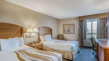Habitación de hotel con dos camas, un escritorio, una silla, un teléfono y una ventana con cortinas.
