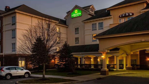 A hotel with a prominent sign, a covered entrance, and a car parked in front. - La Quinta Inn & Suites by Wyndham Islip - MacArthur Airport (Bohemia)