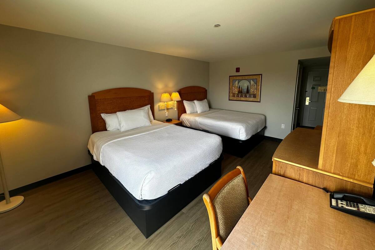 Une chambre d’hôtel avec deux lits, un bureau, une chaise et une lampe.