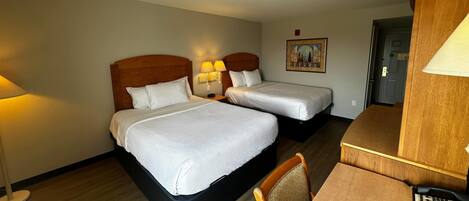A hotel room with two beds, a desk, a chair, and a lamp.
