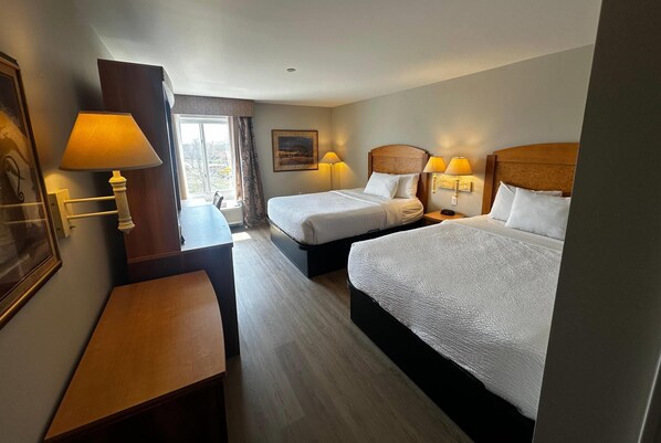 Habitación de hotel con dos camas, un escritorio y una ventana con cortinas.
