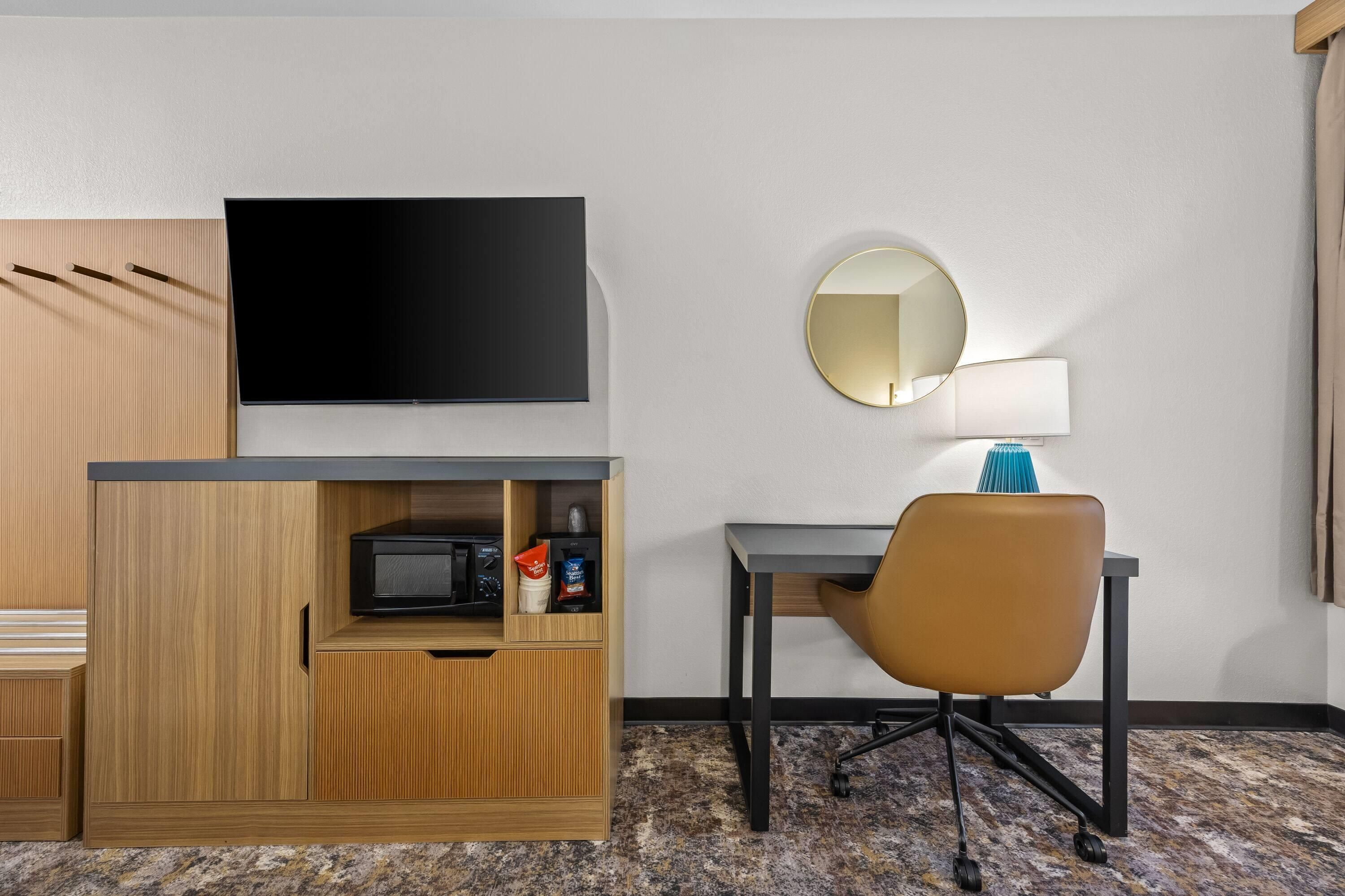 Een hotelkamer met een flatscreen televisie, een ronde spiegel, een bureau, een stoel en een magnetron.