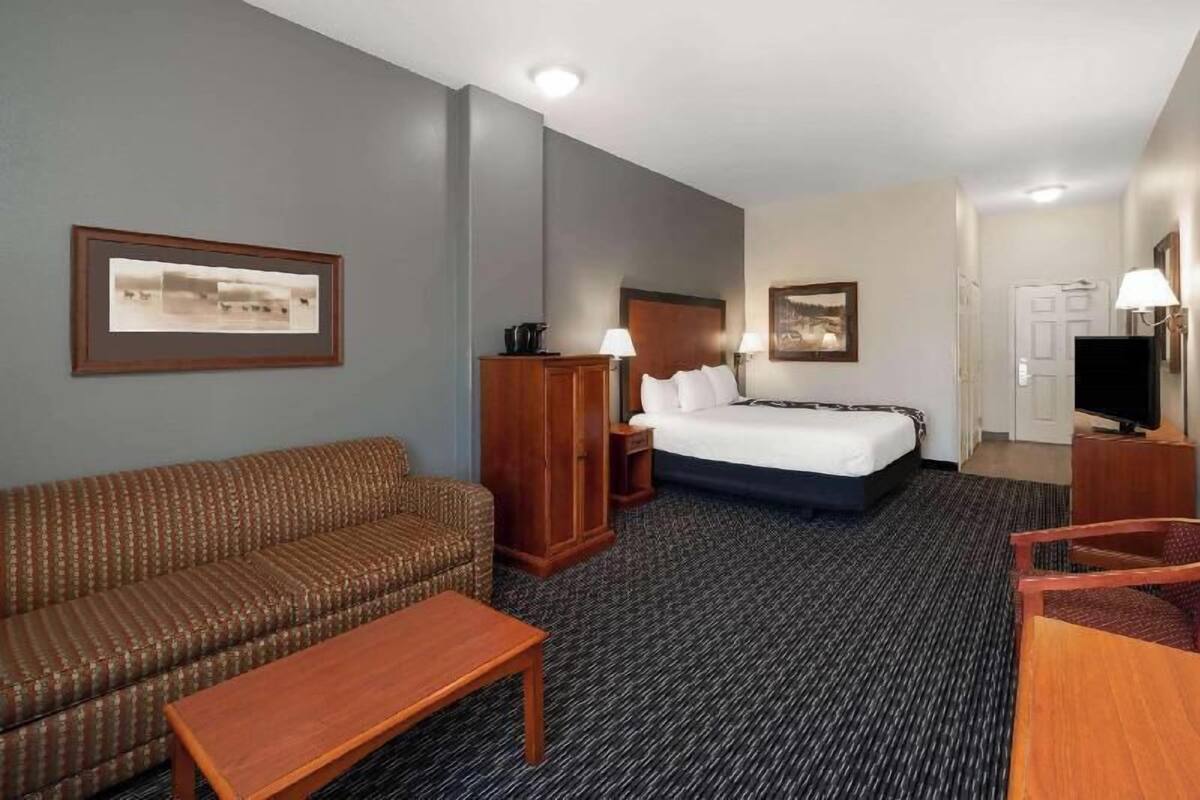 A hotel room with a bed, a sofa, a desk, a TV, and framed pictures on the walls.