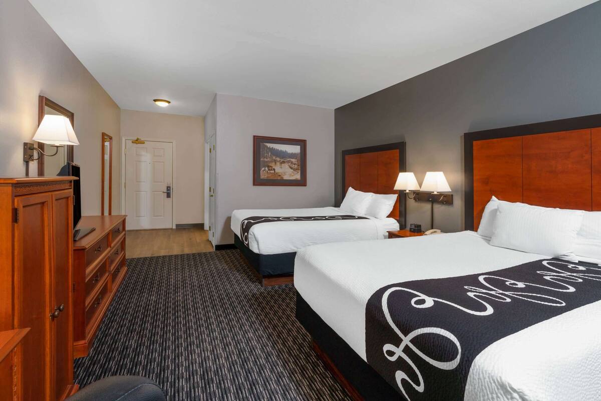 A hotel room with two beds, a dresser, a desk, and a framed picture on the wall.