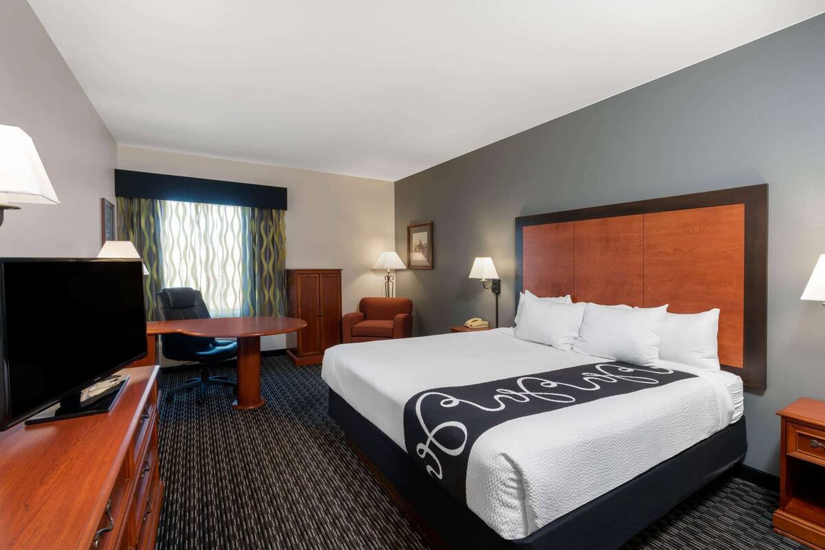 A hotel room with a large bed, a desk, a television, and a chair.