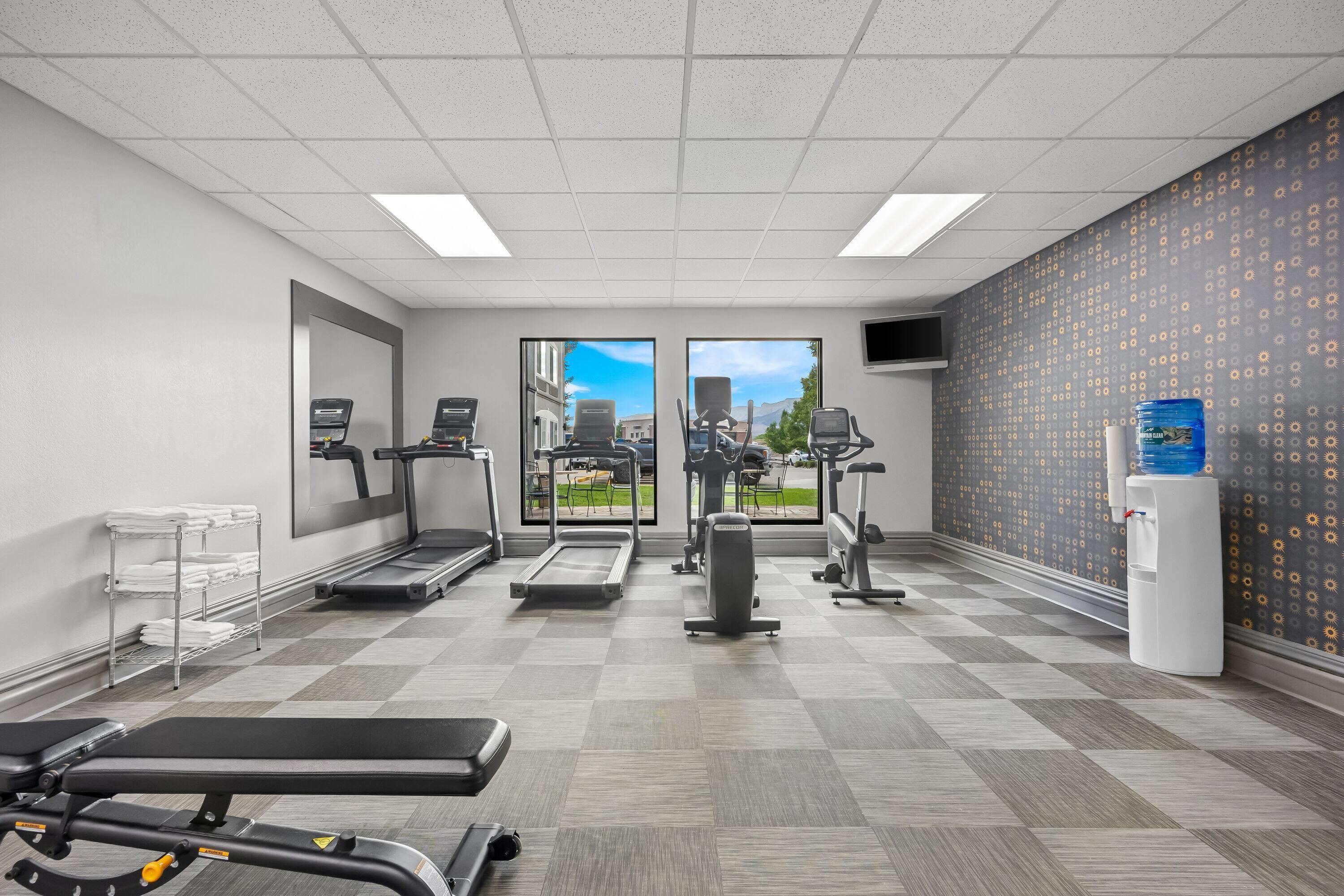A gym with treadmills, elliptical machines, a bench press, and a water dispenser.