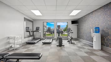 A gym with treadmills, elliptical machines, a bench press, and a water dispenser.