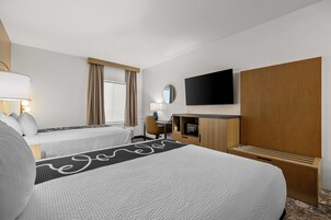 Habitación de hotel con dos camas, un escritorio, un televisor de pantalla plana y un panel de pared de madera.