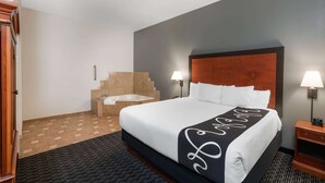 A hotel room with a large bed, two bedside lamps, a wooden headboard, a bathroom with a bathtub, and a carpeted floor. - La Quinta Inn & Suites by Wyndham Rifle (Rifle)