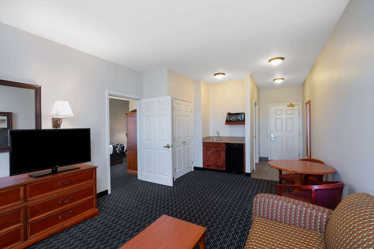 A hotel room with a TV, wooden furniture, a small dining table, and a kitchenette.