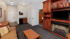 A living room with a fireplace, television, and wooden cabinets. - La Quinta Inn & Suites by Wyndham Rifle (Rifle)