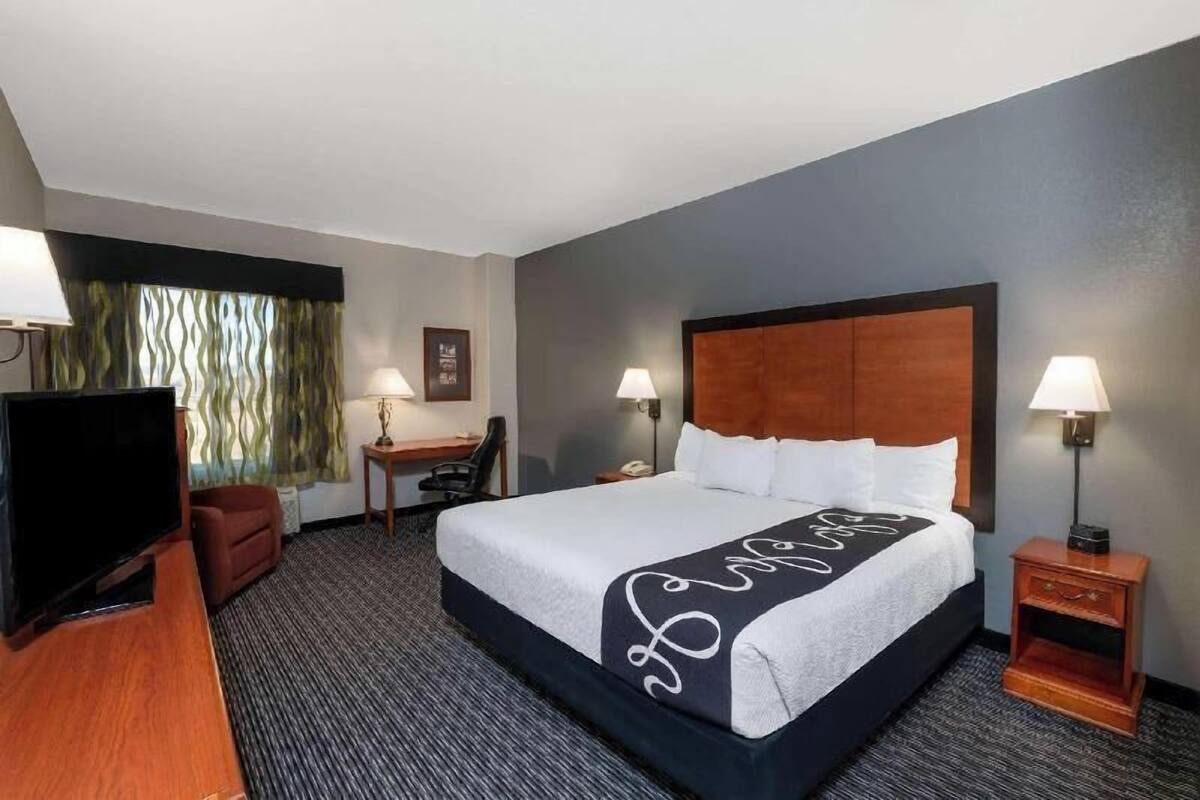 A hotel room with a large bed, a desk, a television, and two lamps.