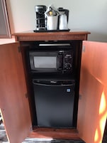 Una kitchenette compacta con cafetera, microondas y refrigerador pequeño.