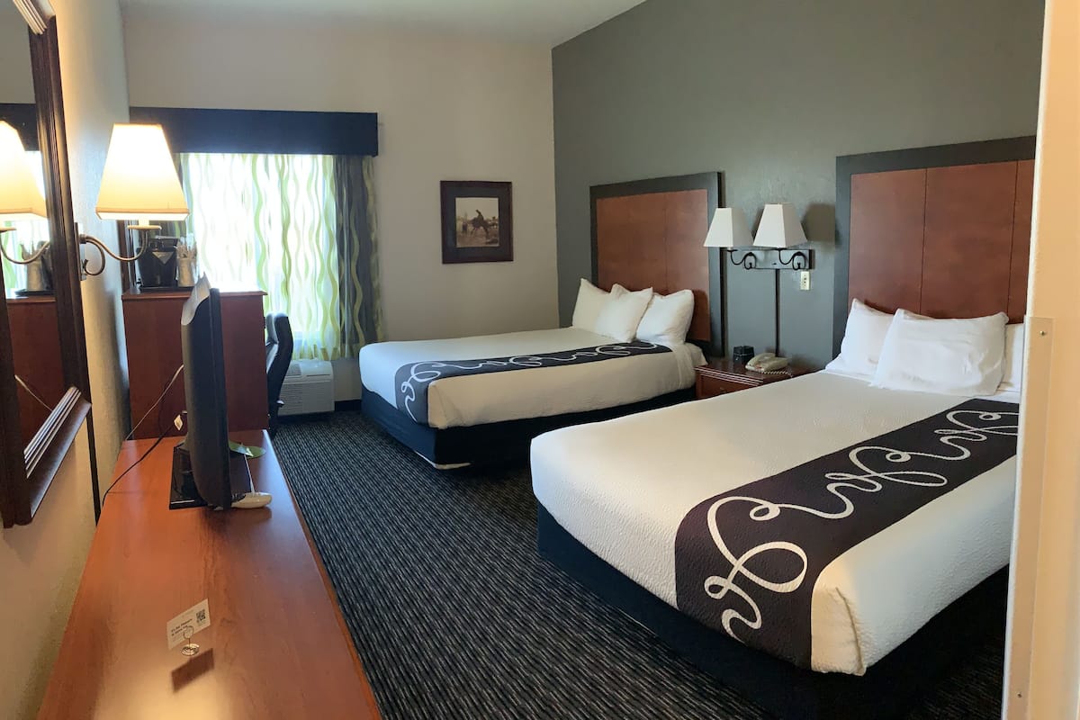 A hotel room with two beds, a desk, a chair, and a television.
