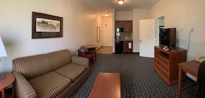 A living room with a sofa, a small table, a TV, and a kitchen area with cabinets and a microwave.