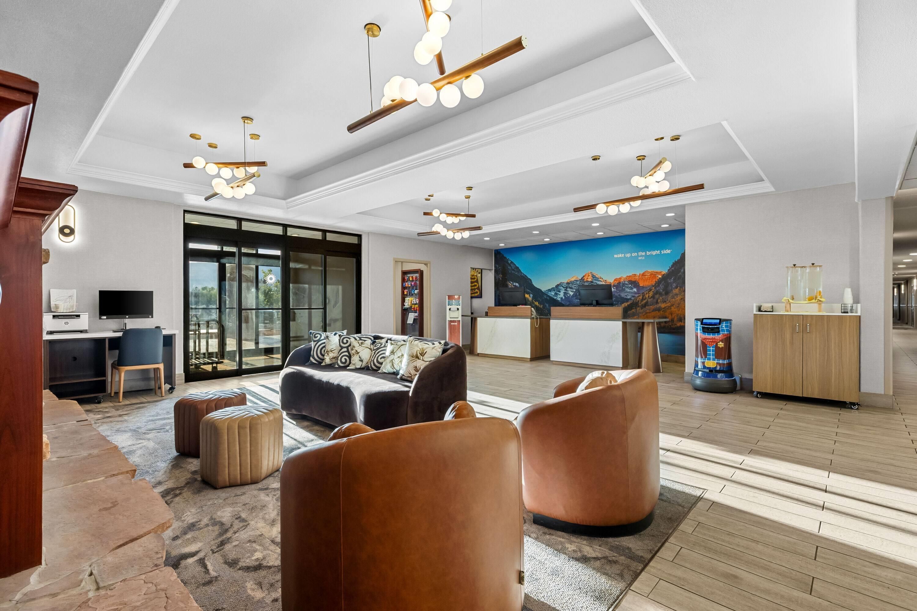 A modern hotel lobby with a reception desk, seating area, and a large window.