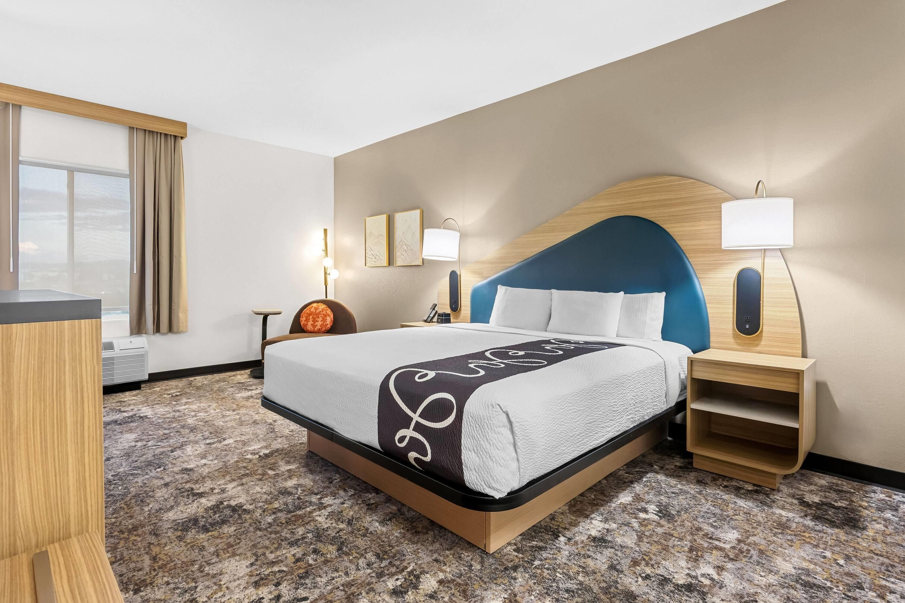 A hotel room with a bed, bedside tables, a desk, and a window with curtains.