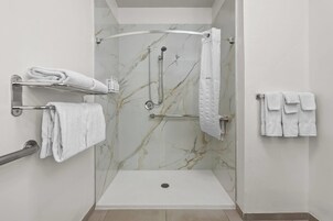 A modern shower area with a marble wall, a handheld showerhead, a glass-enclosed shower, and multiple towel hooks.