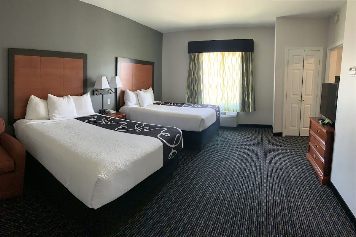 A hotel room with two beds, a chair, a lamp, a dresser, and a television.