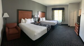 Une chambre d’hôtel avec deux lits, une chaise, une lampe, une commode et un téléviseur.