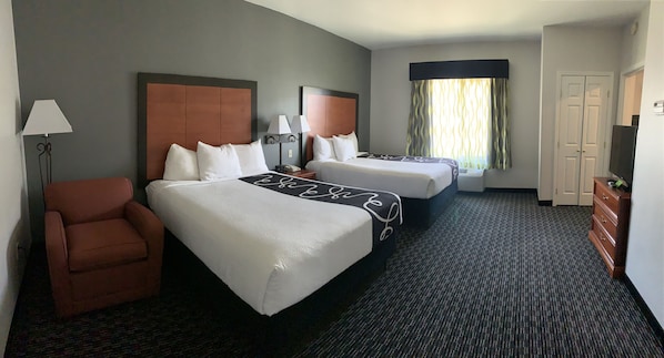 A hotel room with two beds, a chair, a lamp, a dresser, and a television.