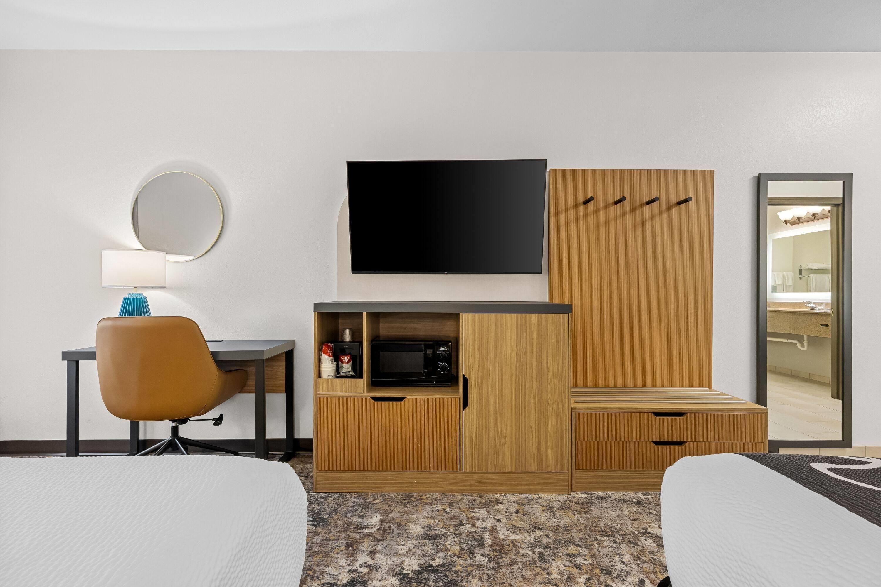 Una habitación de hotel con cama, escritorio con silla, televisor, microondas y armario.