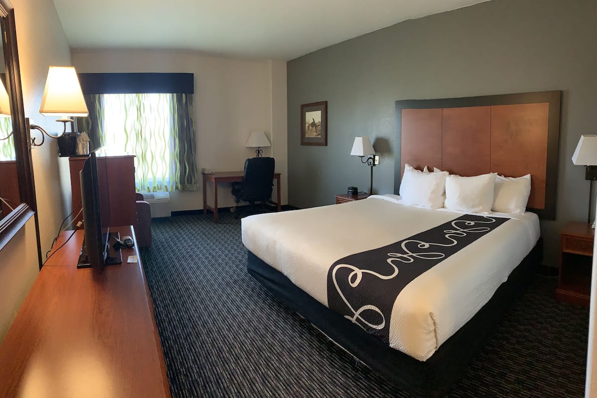 A hotel room with a large bed, a desk, a chair, and a window with curtains.