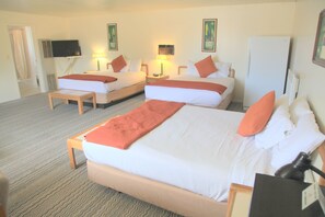 Una habitación de hotel con dos camas, televisión, refrigerador y escritorio con lámpara.