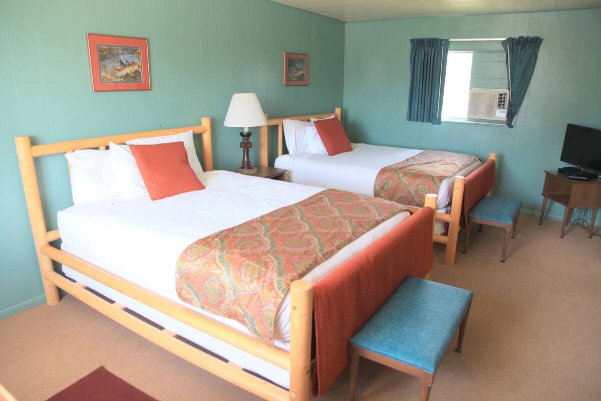 A hotel room with two beds, a desk, a chair, and a television.