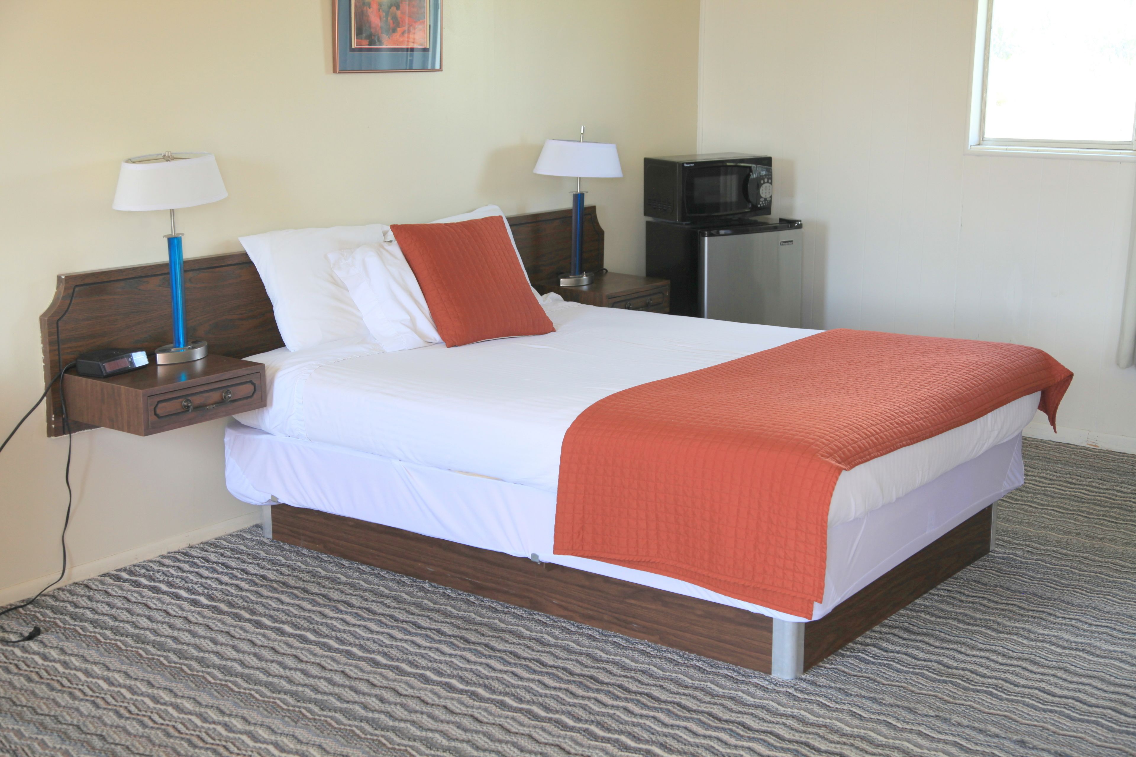 Una cama bien hecha con ropa de cama blanca y naranja, un cabecero de madera y dos mesitas de noche con lámparas.