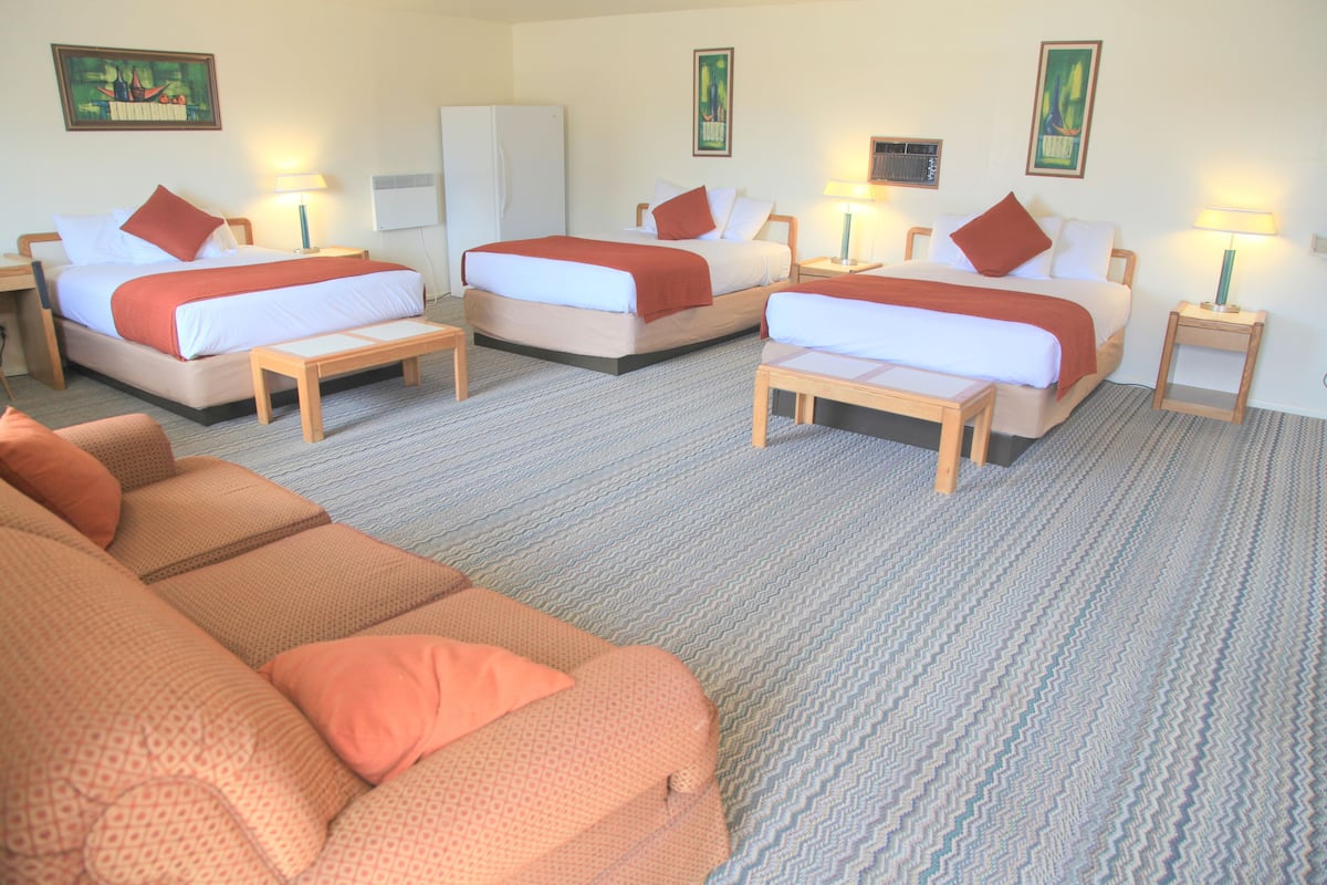 A hotel room with three single beds, a sofa, and a refrigerator.