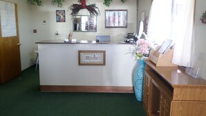 Un área de recepción con un mostrador de madera, un cartel de bienvenida, un espejo y una ventana con cortinas.