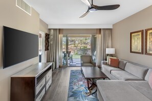 A hotel room with a flat-screen TV, a sofa, a coffee table, a desk, and a ceiling fan. - Hilton Grand Vacations Club Kohala Suites Waikoloa (Waikoloa)