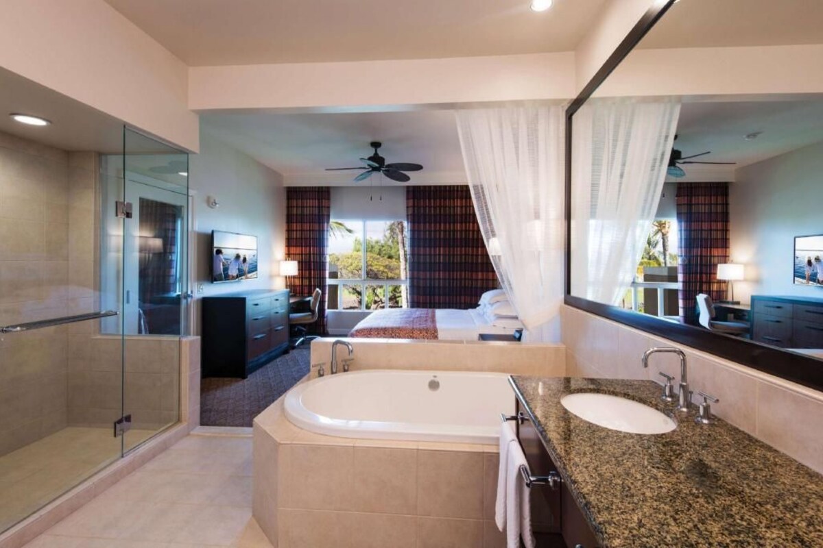 Een moderne hotelkamer met een ruim bad, een aparte douche, een grote spiegel en uitzicht op het groen.