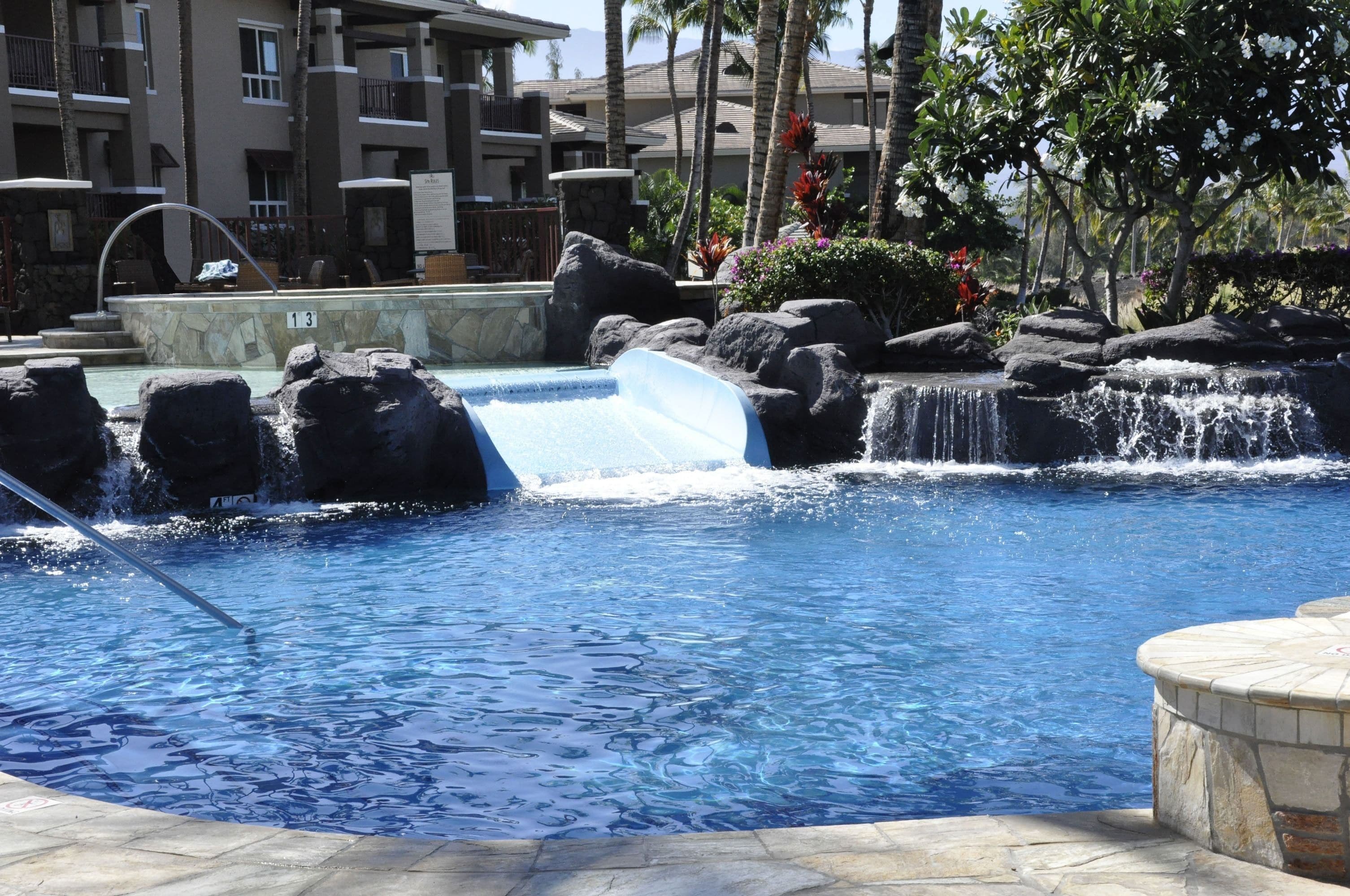A pool with a waterfall feature, surrounded by rocks and palm trees.