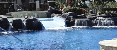A pool with a waterfall feature, surrounded by rocks and palm trees.
