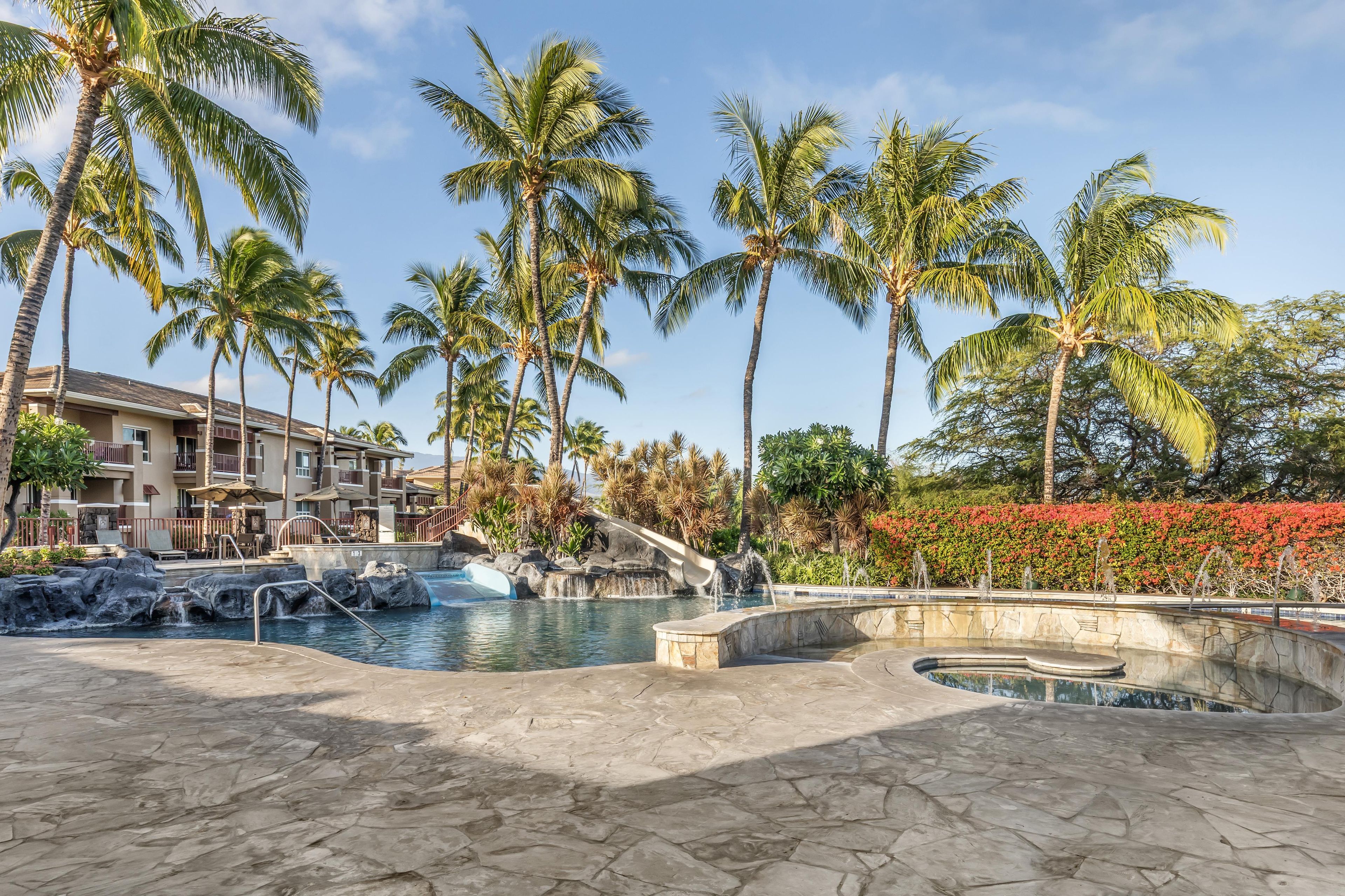Ein Poolbereich eines Resorts mit Palmen, einem Wasserfall und einem Gebäude mit Balkonen.